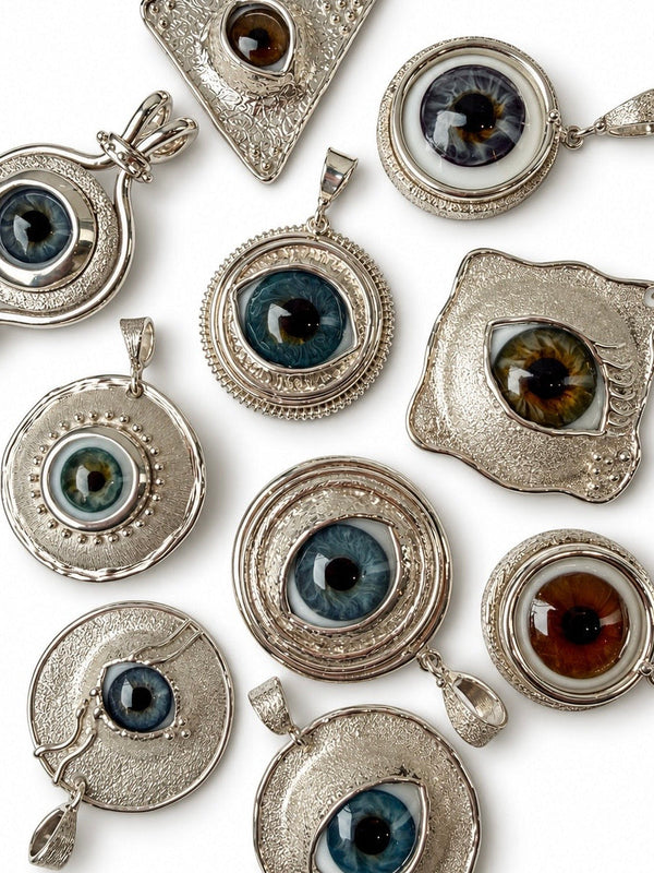 A collection of silver-toned eye pendants with various realistic colored irises, arranged on a plain white background.